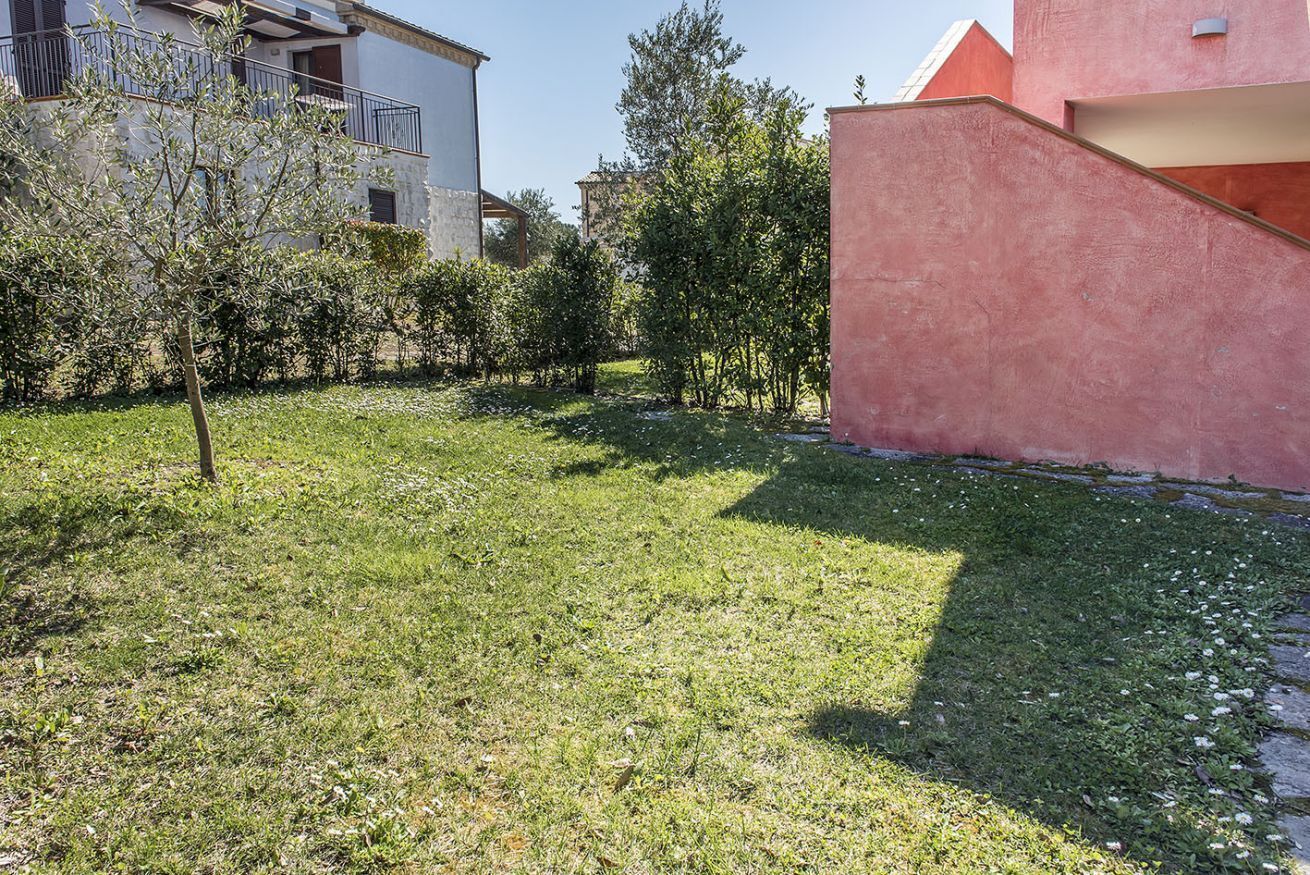 Un patio cubierto de césped con un árbol, un edificio con balcón y una pared rosa.
