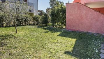 Un patio cubierto de césped con un árbol, un edificio con balcón y una pared rosa.