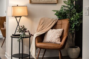 Ein brauner Ledersessel mit einer Decke und einem Kissen, eine Stehlampe und ein Blumentopf.