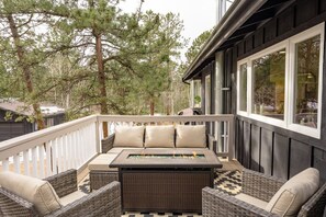 Eine Terrasse im Freien mit Korbmöbeln, einem Feuerkorb und Blick auf Bäume.