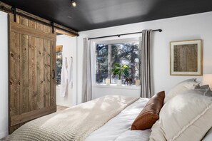 A bedroom with a large wooden wardrobe, a bed with white bedding, a window with curtains, and a framed picture on the wall.