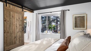 Ein Schlafzimmer mit großem Holzschrank, einem Bett mit weißer Bettwäsche, einem Fenster mit Vorhängen und einem gerahmten Bild an der Wand.