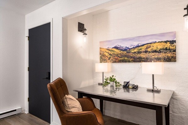 Un coin repas comprenant une table, deux lampes, une chaise et un tableau accroché au mur.