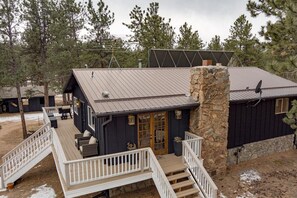 A cabin with a stone chimney, a deck with railings, and a covered outdoor seating area.