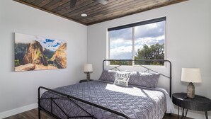 Quarto com cama, janela com vista, ventilador de teto e um quadro na parede.
