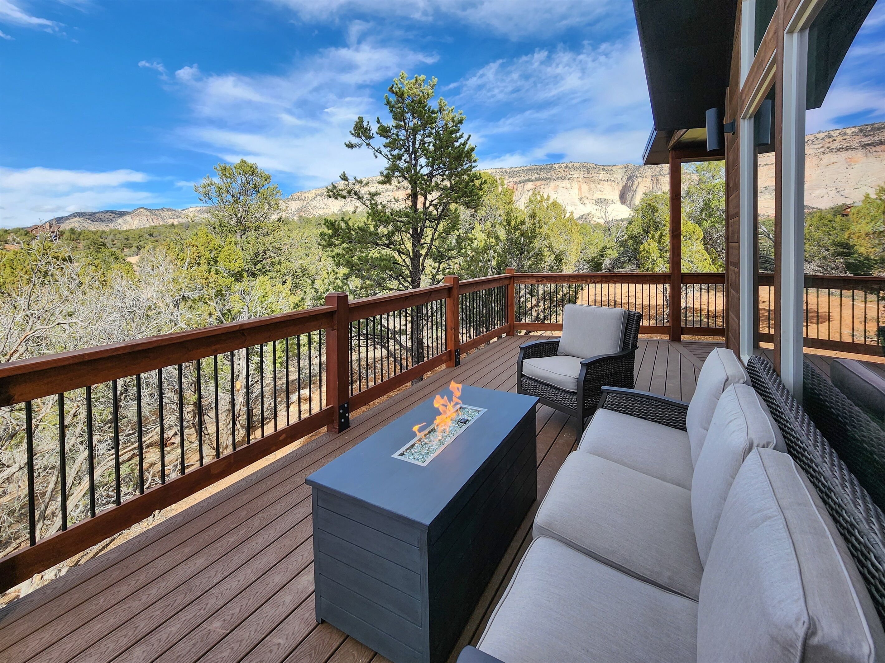 A wooden deck with outdoor furniture, including a sofa and chairs, overlooking a mountainous landscape.