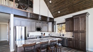 A spacious kitchen with a large island, dark wood cabinets, stainless steel appliances, and a high ceiling with exposed beams. - Stargazer Cabin | Private Hot tub | Zion NP (Orderville)
