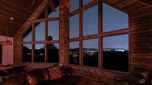 A log cabin interior with large windows offering a starry night sky view. - Stargazer Cabin | Private Hot tub | Zion NP (Orderville)