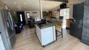 A modern kitchen with a central island, stainless steel appliances, and a large window. - Modern Ranch Studio With a Beautiful Round Porch (Cocoa)