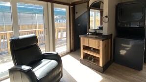 A spacious living area with a black leather chair, wooden entertainment unit, and a black refrigerator. - Modern Ranch Studio With a Beautiful Round Porch (Cocoa)