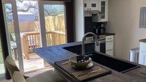 A modern kitchen with a wooden island, stainless steel appliances, and a sliding glass door leading to a deck. - Modern Ranch Studio With a Beautiful Round Porch (Cocoa)