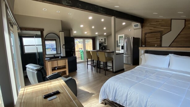 A modern hotel room with a large bed, a desk with a chair, a kitchenette, and a bathroom. - Modern Ranch Studio With a Beautiful Round Porch (Cocoa)