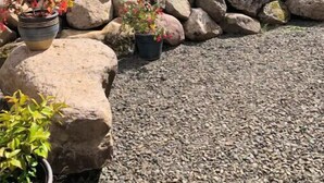 Un jardin avec un chemin de gravier, de gros rochers et des plantes en pot.