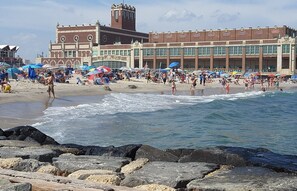 A beach with a large building in the background, featuring a clock tower and multiple windows. - Beautifully restored full home, 5 min to NJ Shore! (Neptune City)