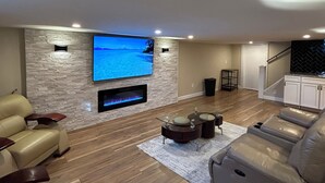Un salon moderne avec un mur en pierre, un téléviseur à écran plat, une cheminée, des canapés en cuir et un escalier.