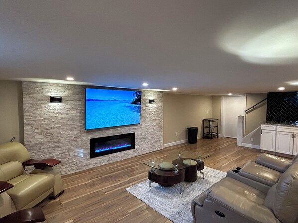 A modern living room with a stone wall, a flat-screen TV, a fireplace, leather sofas, and a staircase. - Beautifully restored full home, 5 min to NJ Shore! (Neptune City)