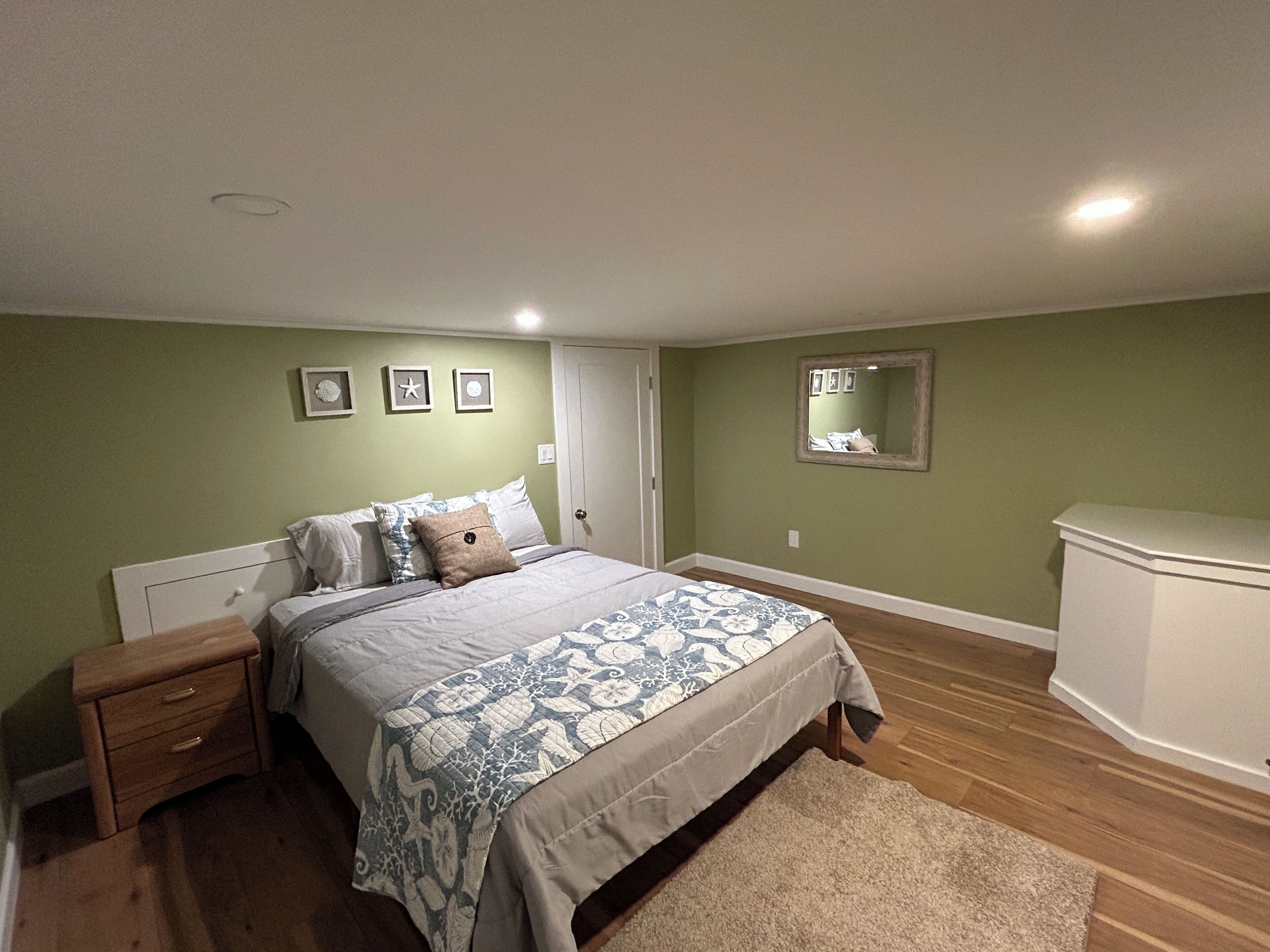 Une chambre à coucher avec un lit, une table de chevet, une commode et un miroir au mur.