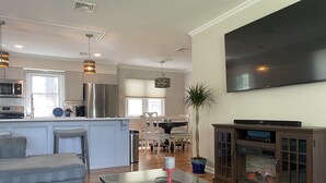 Un salon moderne avec une table basse en verre, une cheminée, un téléviseur et une cuisine en arrière-plan.