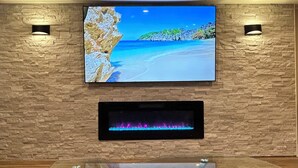 Un salon moderne avec un téléviseur à écran plat fixé à un mur en pierre, une table basse avec un plateau en verre et une cheminée en dessous.