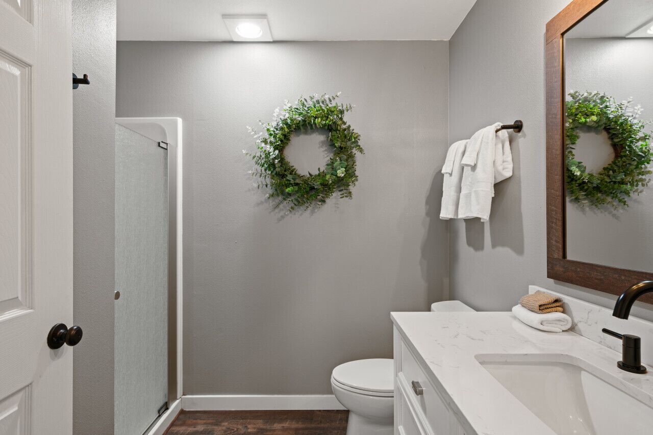 Une salle de bain avec des toilettes blanches, un lavabo avec un miroir et deux couronnes vertes accrochées au mur.