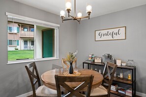A dining area with a round table, chairs, a chandelier, a window with a view of a building, and a 'Grateful' sign on the wall. - Abenteuer Haus in downtown Leavenworth! (Leavenworth)