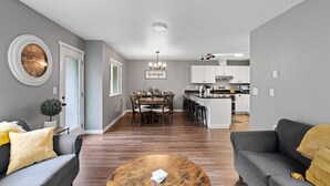 En moderne stue med et rundt sofabord, grå sofaer og et spiseområde med en lysekrone.
