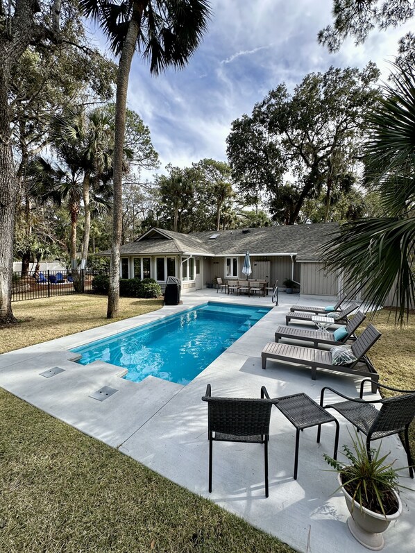 Una piscina con sillones reclinables y un patio cubierto.
