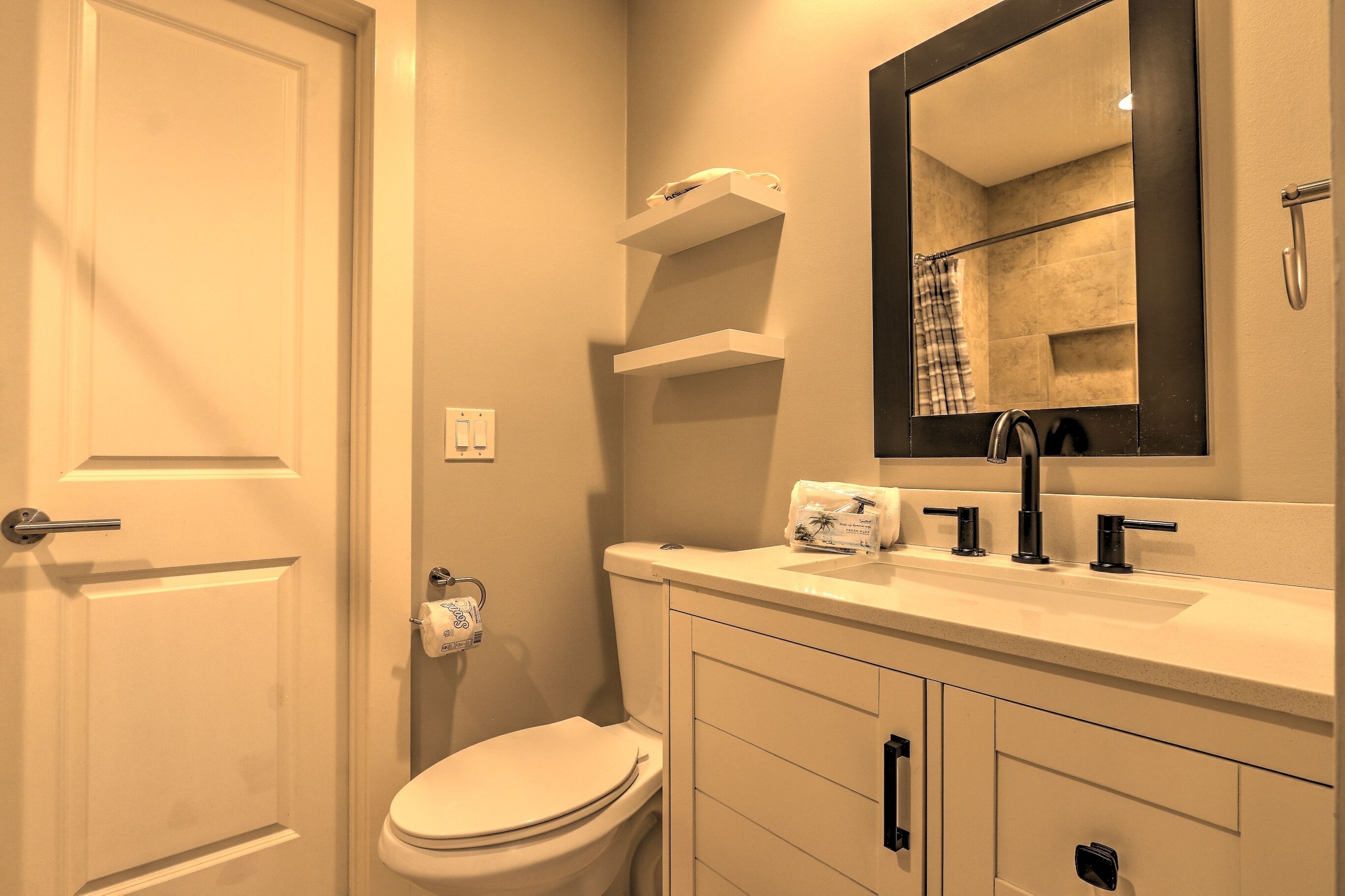 A bathroom with a toilet, sink, mirror, towel rack, and towel dispenser.