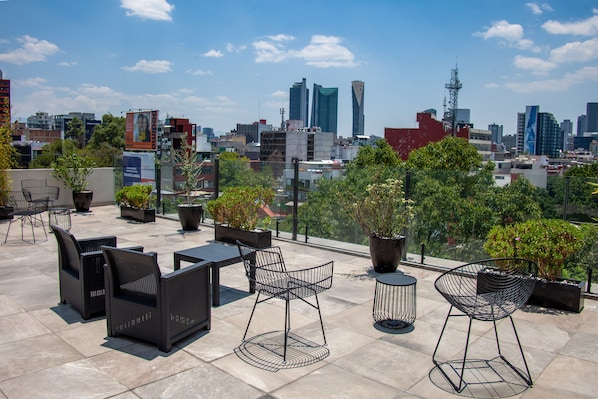 Eine Dachterrasse mit Gartenmöbeln und Blumentöpfen, mit Blick auf eine Skyline moderner Gebäude.