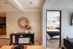 Ein modernes Hotelzimmer mit einem großen Bett, einem Schreibtisch mit Spiegel und Blick in ein weiteres Zimmer.