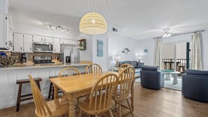 A modern kitchen with white cabinets, a wooden dining table, and a hanging light fixture. - BEACH-FRONT CONDO, OUTDOOR POOL, PRIVATE BALCONY! (Gulf Shores)