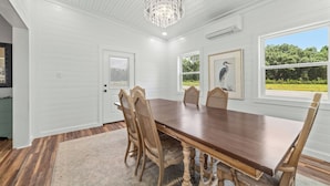 Ruokailuhuoneessa on puinen pöytä ja tuolit, kattokruunu sekä seinillä olevia taideteoksia kehyksissä.