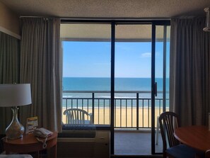 Habitación de hotel con vista a la playa, una mesa, sillas, una lámpara y un teléfono en la mesita de noche.