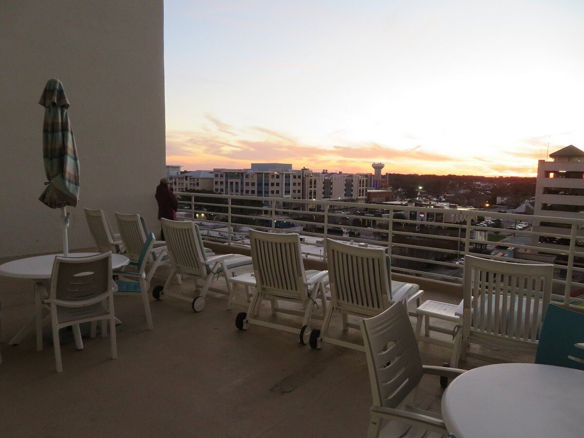Ein Balkon mit weißen Stühlen und einem Tisch, mit Blick auf eine Stadtlandschaft bei Sonnenuntergang.