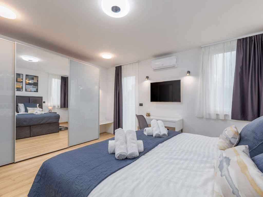 A modern hotel room with a large bed, a desk, a TV, and a wardrobe.