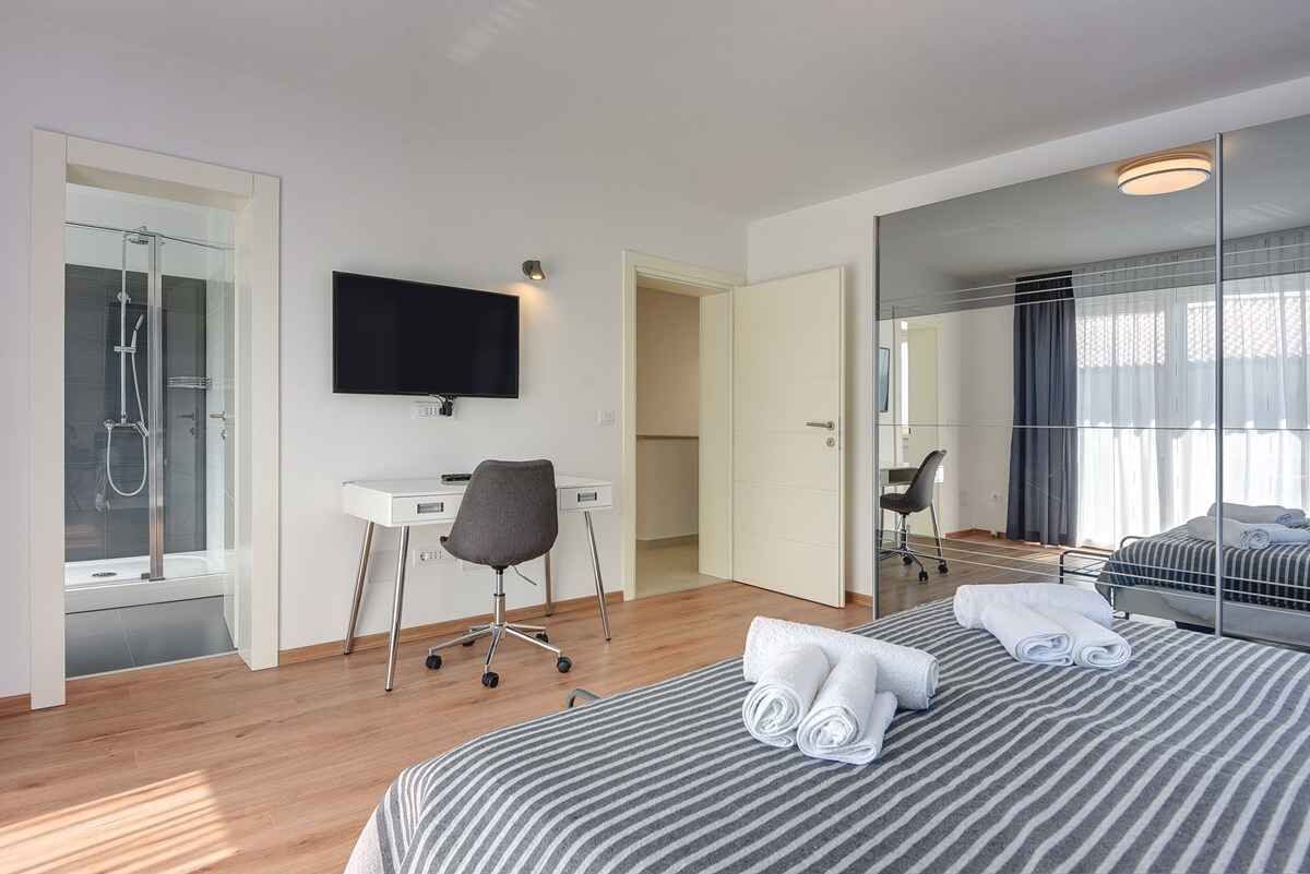 Une chambre d’hôtel moderne équipée d’un lit, d’un bureau, d’une chaise, d’une télévision, d’une douche et d’un grand miroir.