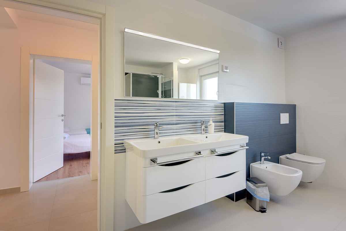 A modern bathroom with a large mirror, two sinks, a bidet, and a walk-in shower.