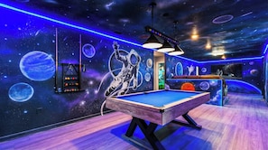 Un tavolo da biliardo con un murale a tema spaziale, e un soffitto illuminato al neon.
