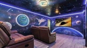 Una stanza con un murale a tema spaziale, una poltrona reclinabile, una poltrona massaggiante e un grande schermo che mostra una scena spaziale.