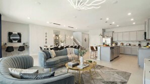En moderne stue med en grå sofa, et rundt sofabord og et spiseområde med en lysekrone.
