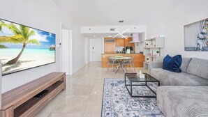 Ein modernes Wohnzimmer mit Flachbildfernseher, einer Couch, einem Couchtisch und einem gemusterten Teppich.