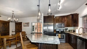 A kitchen with dark wooden cabinets, stainless steel appliances, and a granite countertop. - Gym  Hot Tub & Seasonal Outdoor Pool  Bike Trail  Parking Garage (Park City)
