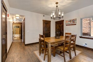 Ein Esszimmer mit Holztisch und -stühlen, einer Kristallleuchter und einem Fenster mit Blick auf eine Ziegelwand.