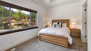 A bedroom with a large window, a ceiling fan, a wooden bed, two bedside tables, and a view of a rocky landscape. - Gym  Hot Tub & Seasonal Outdoor Pool  Bike Trail  Parking Garage (Park City)