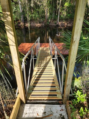 Un ponte di legno che conduce a un molo su un'acqua calma, circondato da vegetazione lussureggiante e alberi.