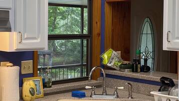 A kitchen with white cabinets, a granite countertop, a stainless steel stove, a window with a view of trees, and a wooden window frame.