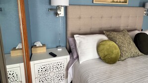 Un dormitorio con cama, mesitas de noche, lámpara, un cuadro y adornos en la pared.