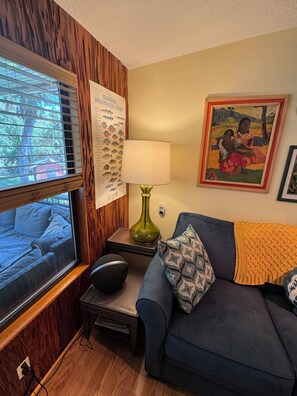 Una stanza con parete rivestita in legno, un poster sui pesci d'acqua dolce della Florida, una lampada, un divano con cuscini decorati e una foto incorniciata.