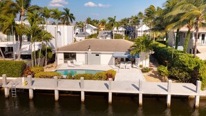 A waterfront property with a swimming pool, lounge chairs, and a covered patio area.
