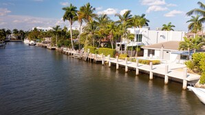A waterfront property with a dock extending into calm water, surrounded by palm trees and modern buildings.